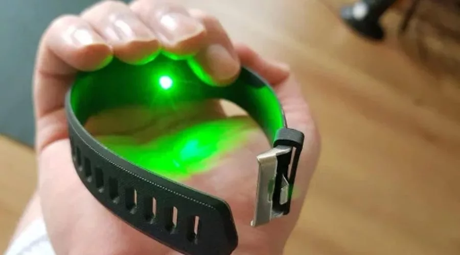 A person holding the SmartTrack watch in hand, showing the green laser at the back of the watch measuring tension.